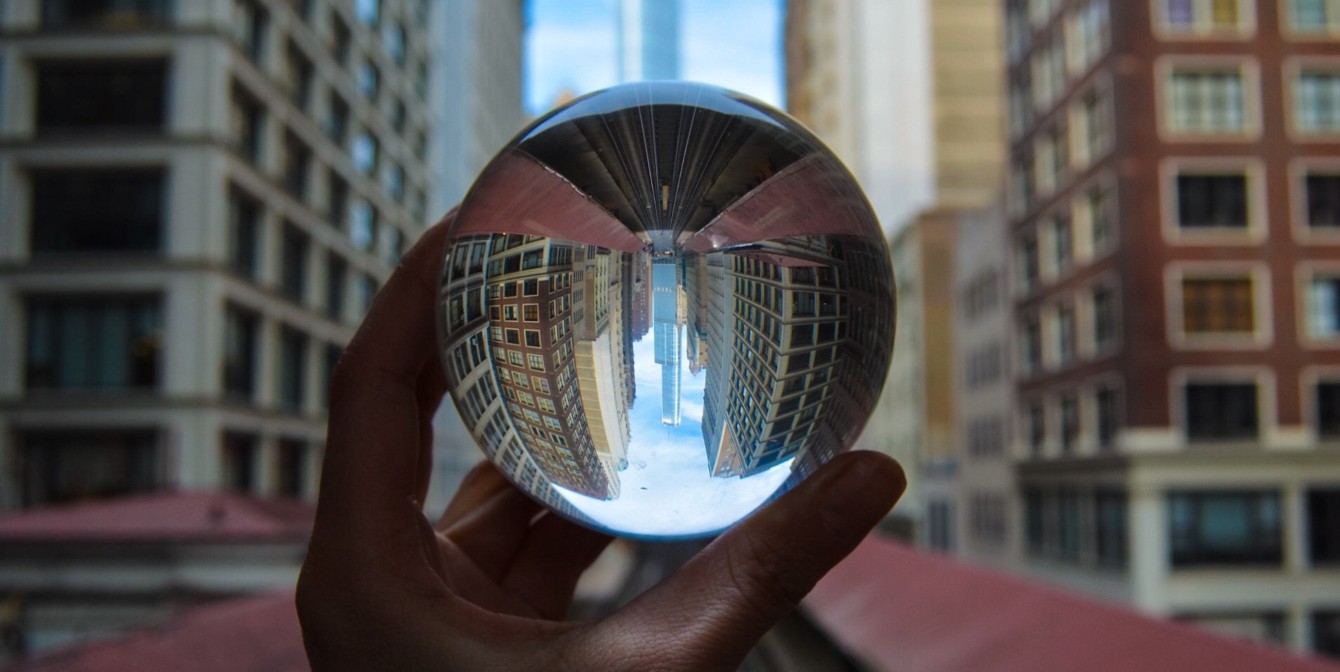 CREspacescrystalball | JLL Technologies a hand holds a crystal ball in the foreground of a city skyline reflecting the buildings