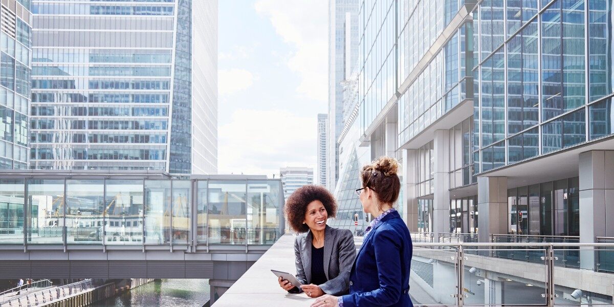 two business women having a conversation outside of buildings in a business district