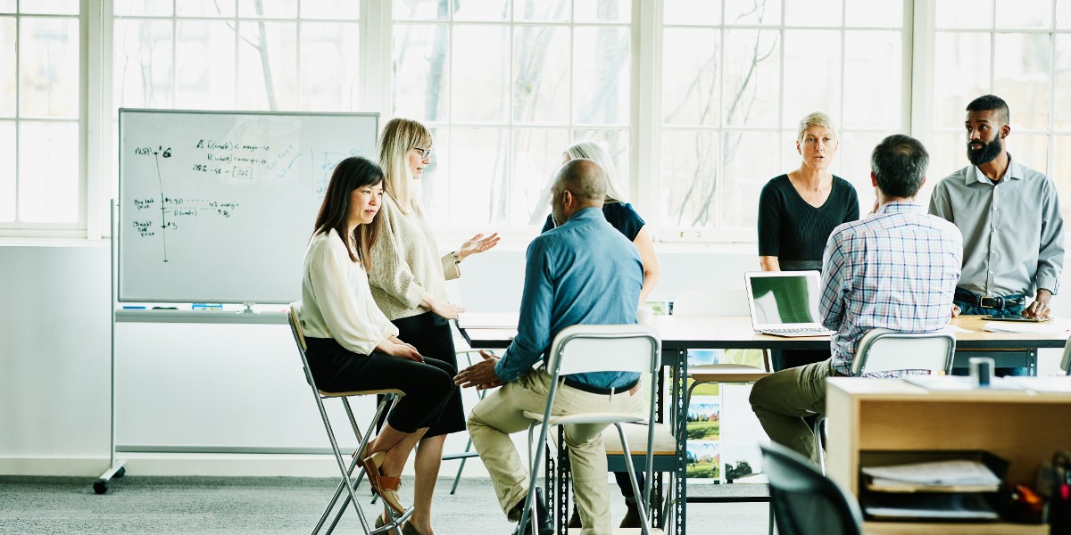 multinational tech co customer story | JLL Technologies business men and women meet around conference table