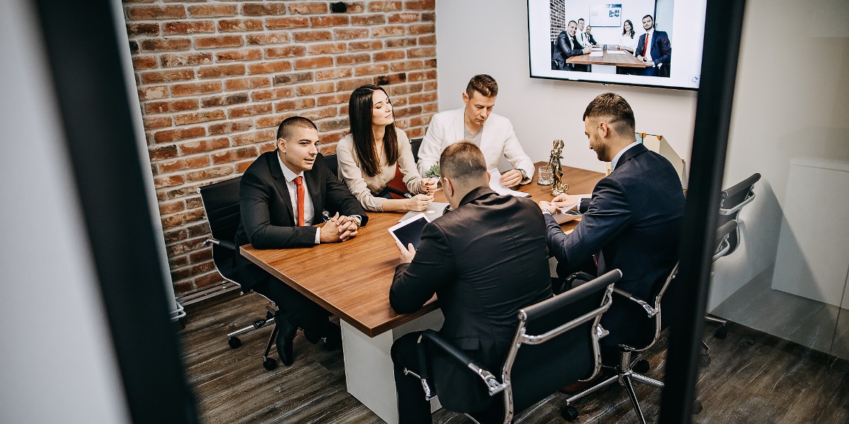 hybridreadymeetingrooms | JLL Technologies business men and woman having a serious conversation in meeting room with virtual team on screen